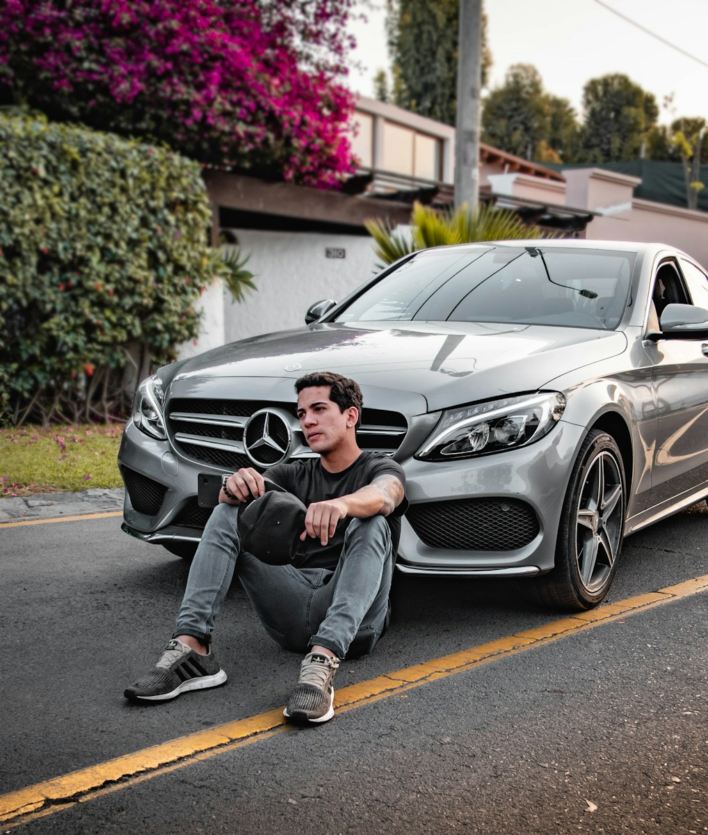 unknown celebrity sitting siting beside silver Mercedes-Benz car outdoors